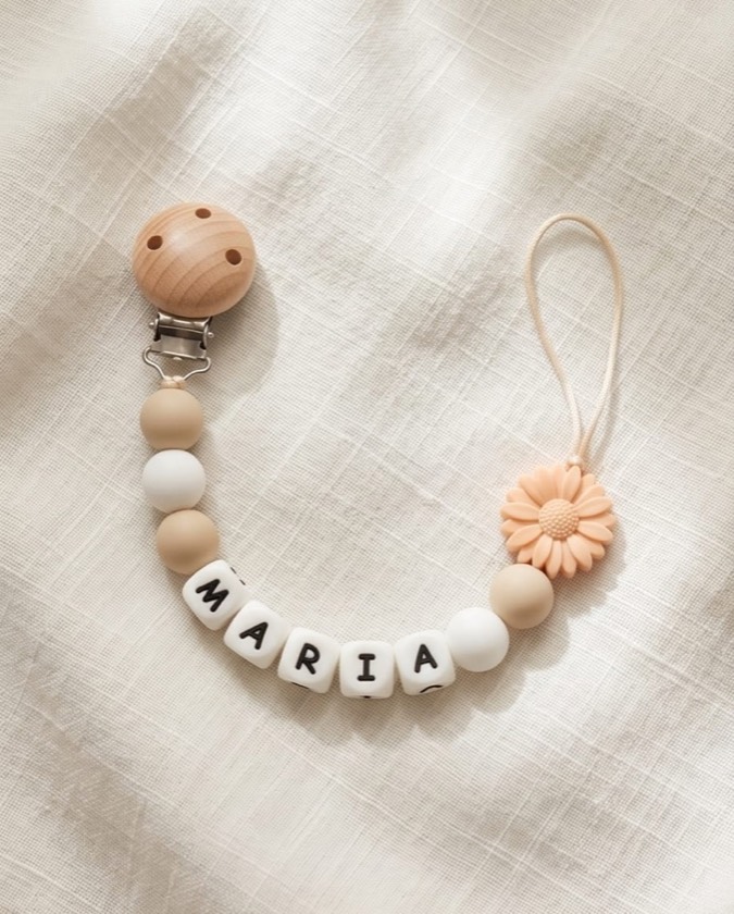 Chupetero con el nombre MARÍA, bolitas beige y blancas y charm de margarita melocotón sobre lino