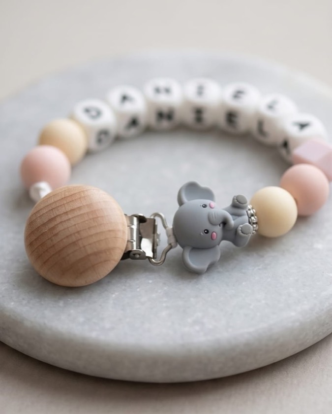 Primer plano de un chupetero rosa con charm de elefante sobre una piedra