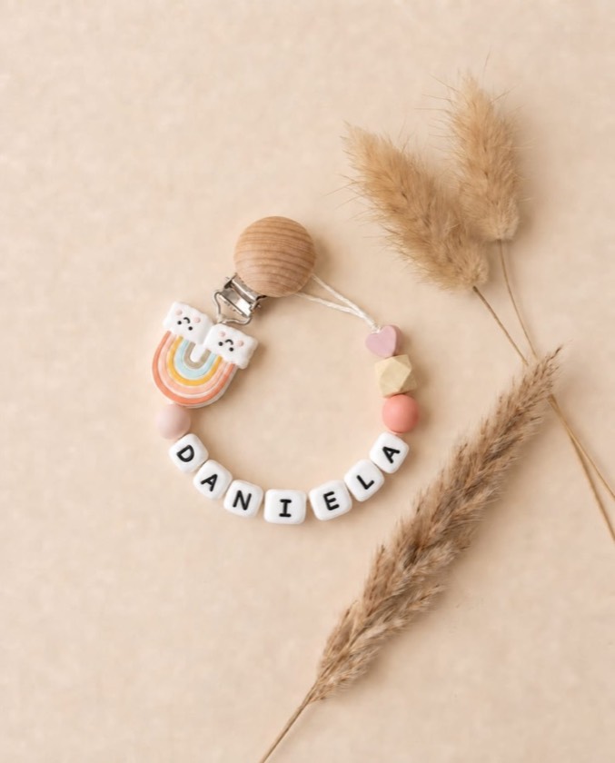 Chupetero con el nombre DANIELA, charm de arcoíris y bolitas rosa y melocotón junto a espigas secas